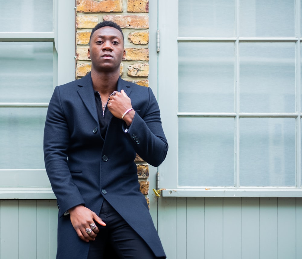 a man in a suit leaning against a brick wall