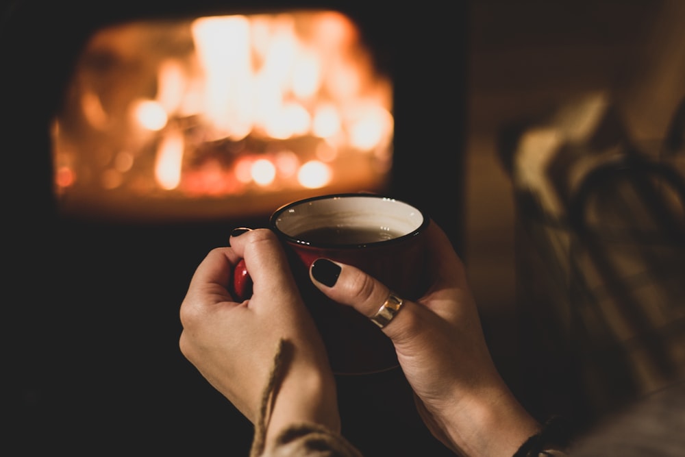 a woman holding a cup of coffee in front of a fireplace