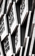 A series of white-framed windows arranged in an asymmetric pattern on a black facade, creating a modern, geometric appearance.