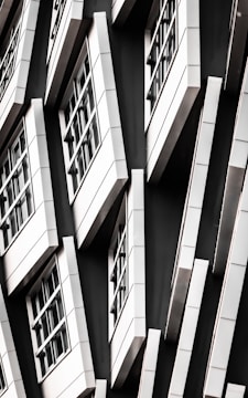 A series of white-framed windows arranged in an asymmetric pattern on a black facade, creating a modern, geometric appearance.