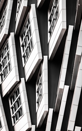 A series of white-framed windows arranged in an asymmetric pattern on a black facade, creating a modern, geometric appearance.