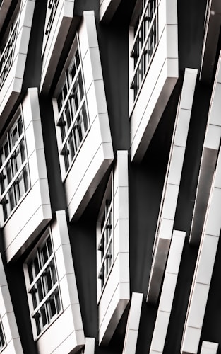 A series of white-framed windows arranged in an asymmetric pattern on a black facade, creating a modern, geometric appearance.
