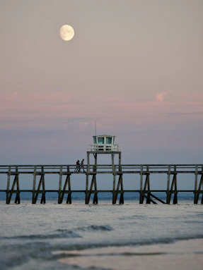 a pier with a lifeguard tower and a full moon in the background