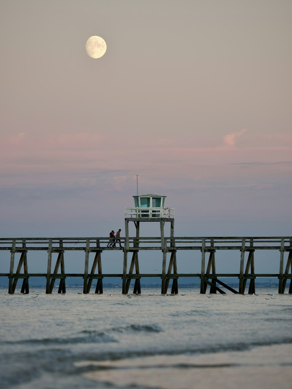 a pier with a lifeguard tower and a full moon in the background