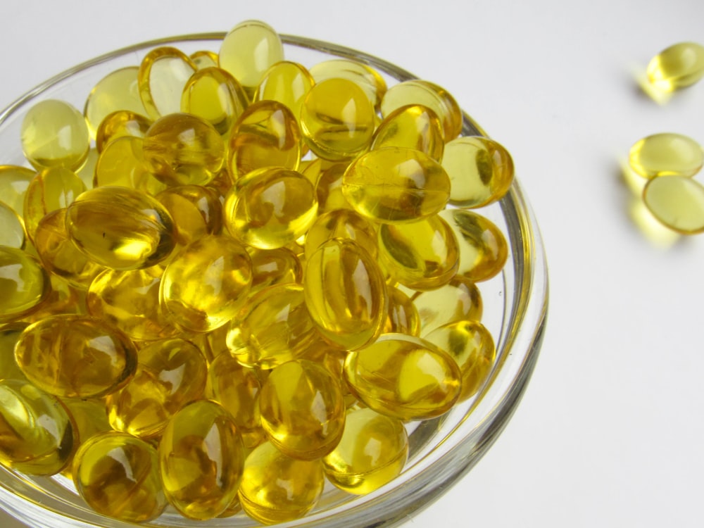 a glass bowl filled with yellow pills on a white surface