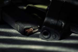 Close-up view of a firearm and ammunition magazine placed on a surface with dim lighting.