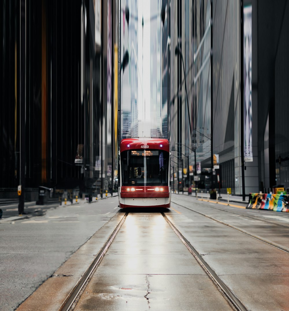 a red and white train traveling down a street next to tall buildings