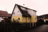 a yellow house with a black roof and a fence