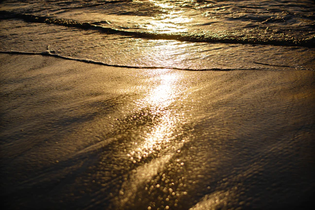 Golden sunlight reflecting off gentle waves on a quiet Greek beach at sunset.