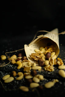 Artfully arranged premium nuts spilling from an elegant green silk pouch onto a green marble surface.