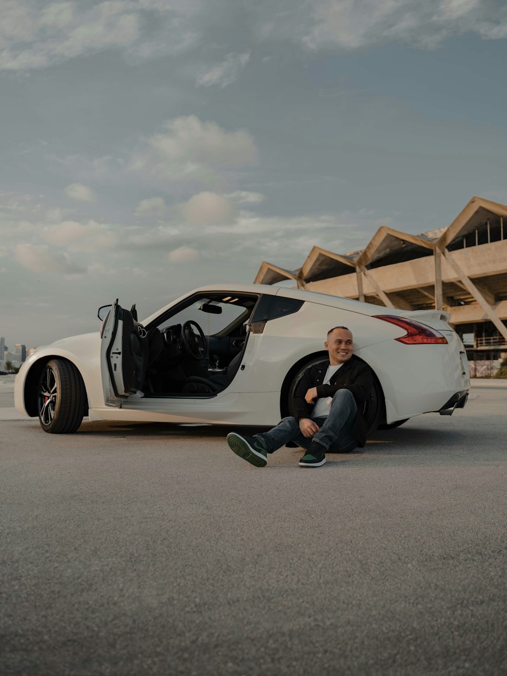 a man sitting on the ground next to a white sports car