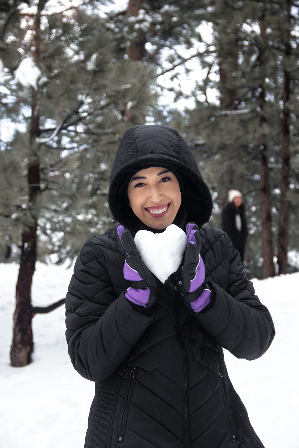 a woman holding a heart shaped snowball in her hands