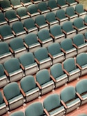 Rows of comfortable auditorium chairs with wooden armrests in a spacious hall.