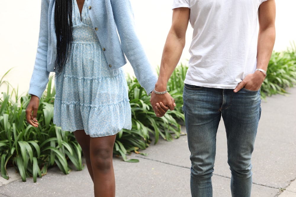 a man and a woman holding hands walking down a sidewalk