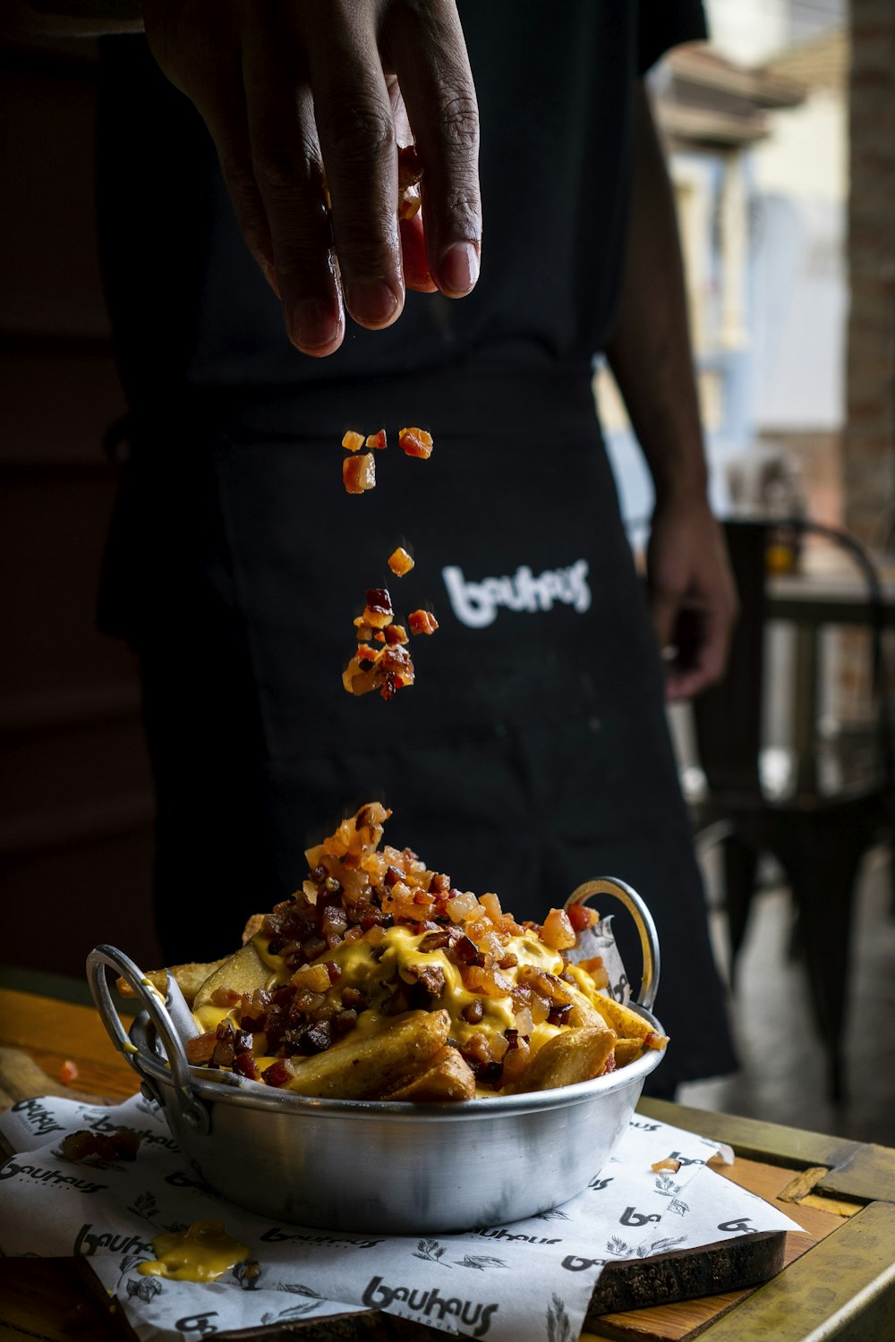 a person is sprinkling chili onto a bowl of french fries
