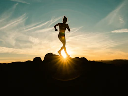 a silhouette of a woman running on a hill at sunset