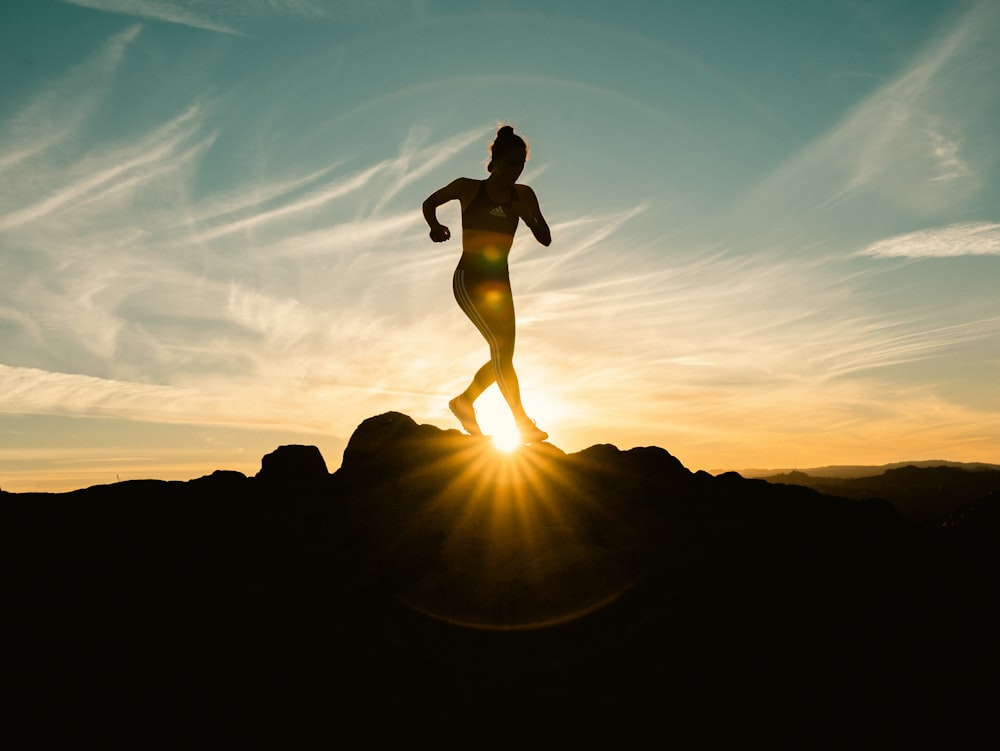 a silhouette of a woman running on a hill at sunset