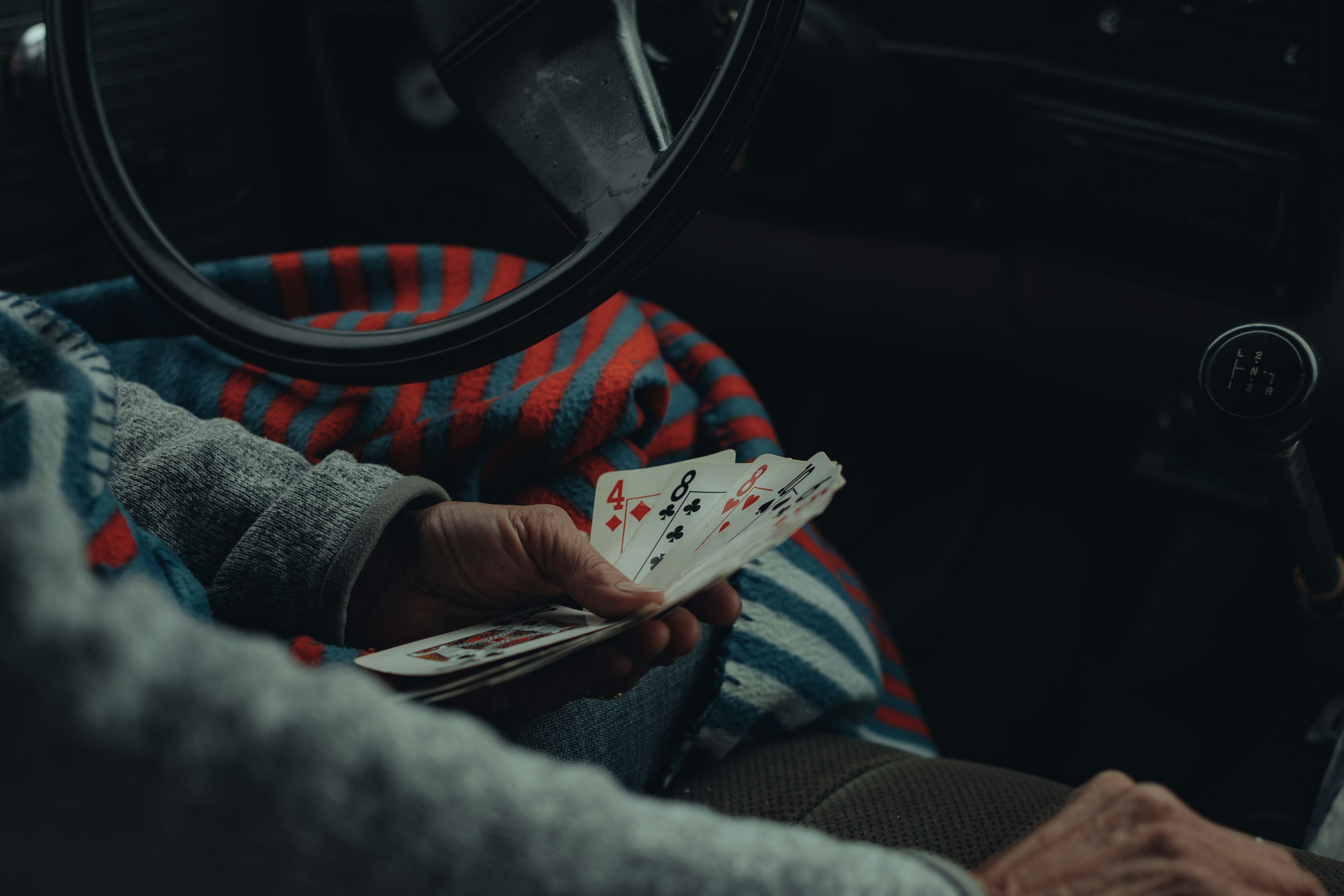 a person sitting in a car holding playing cards