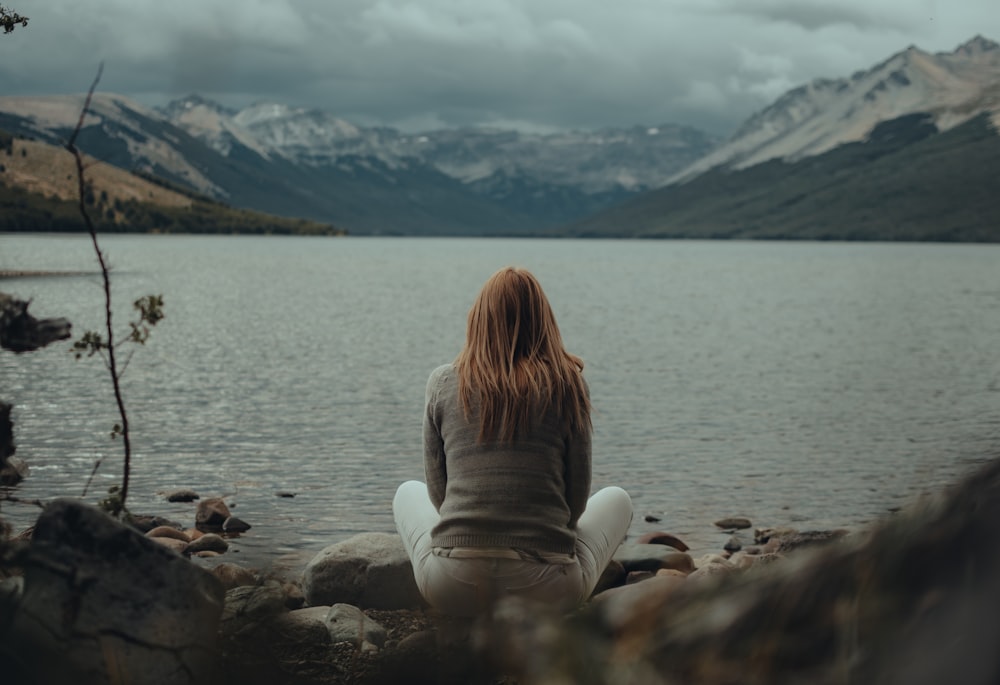 a woman sitting on a rock near a body of water