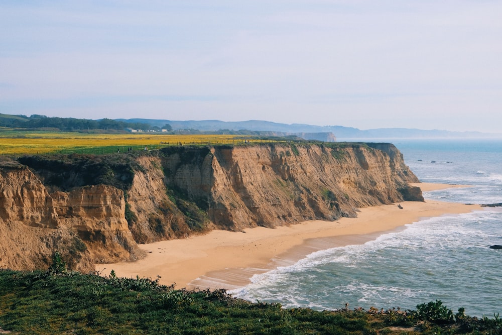 a cliff overlooking the ocean with a sandy beach below