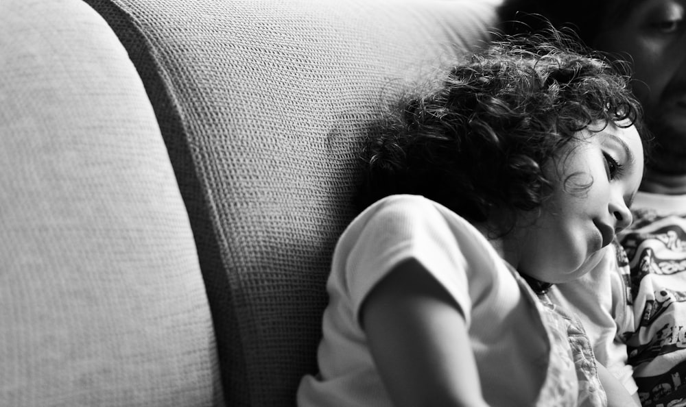 a little girl laying on top of a couch next to a man