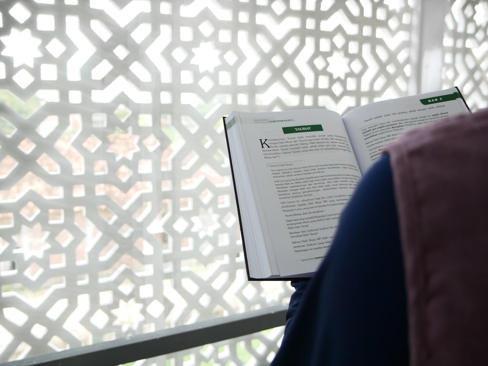 Un libro abierto sentado encima de una silla junto a una ventana