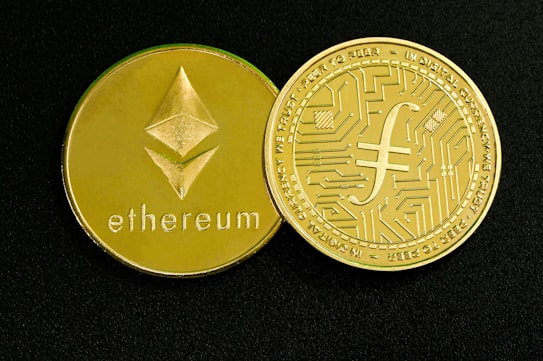 Two gold-colored coins are displayed on a dark surface. One coin features the Ethereum symbol and the word 'ethereum,' while the other has a circuit design and text around the edge.