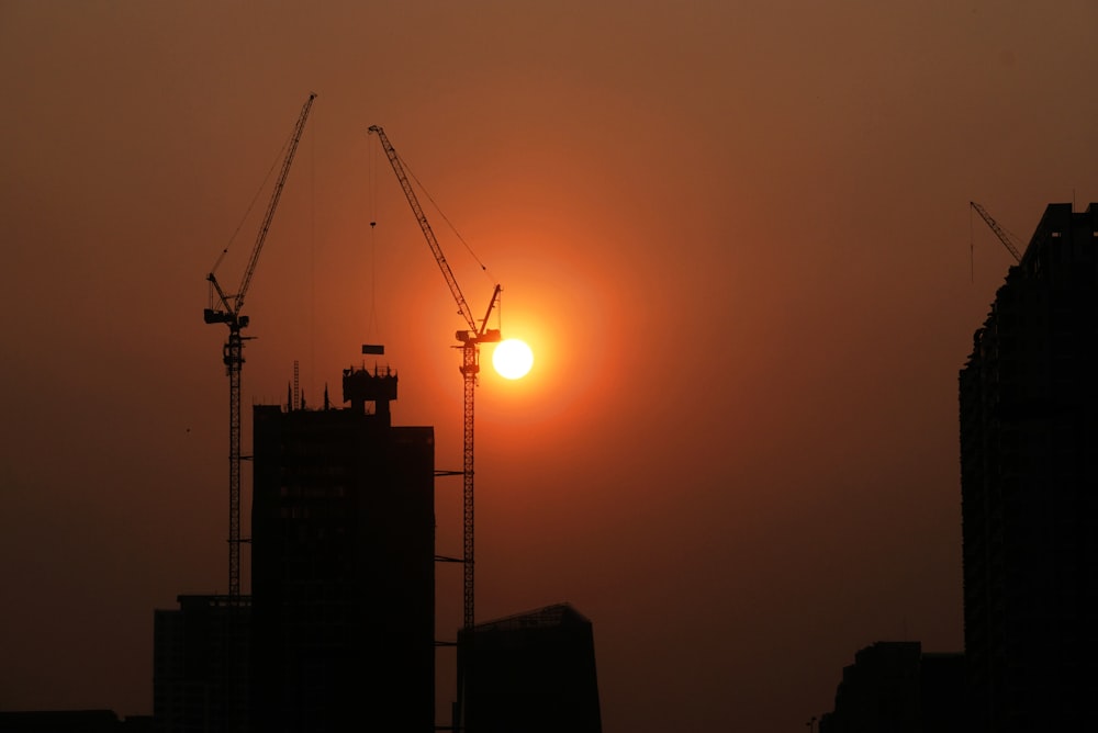 the sun is setting behind some cranes in a city