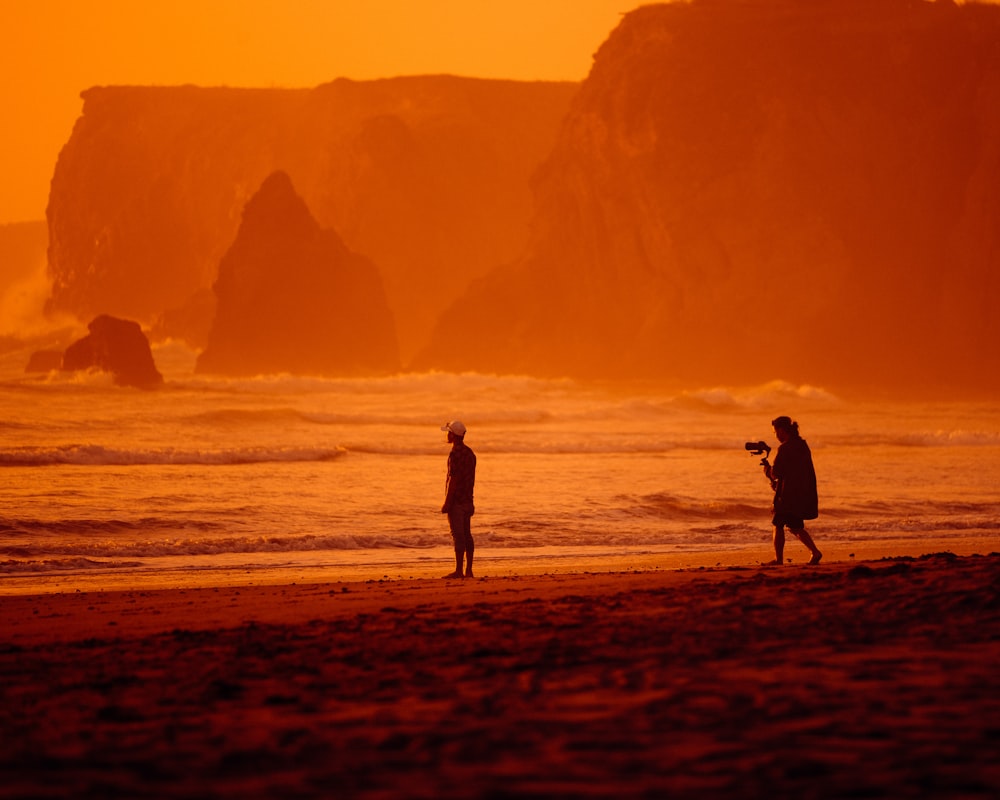 a couple of people standing on top of a sandy beach