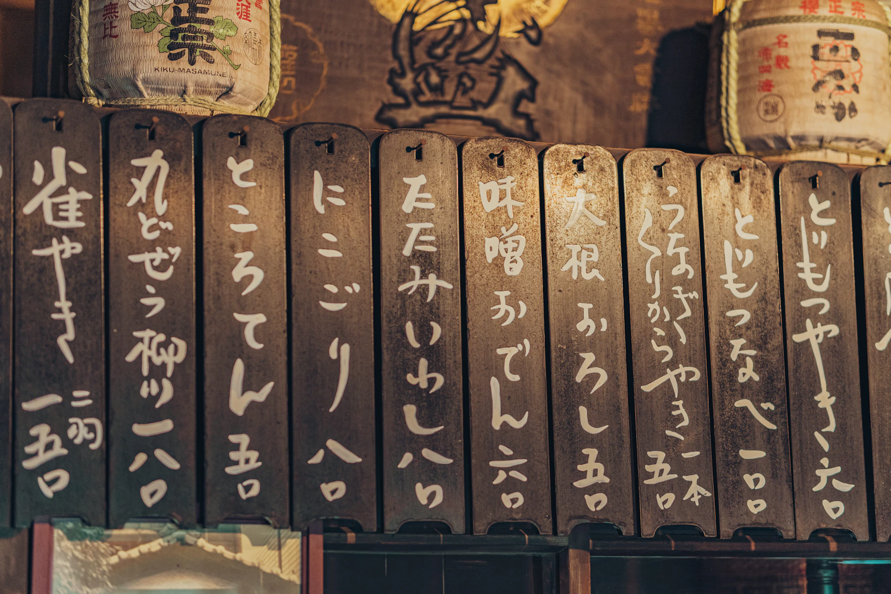 A row of dark wooden menu plaques hand-lettered in white kana, each with a price at the bottom