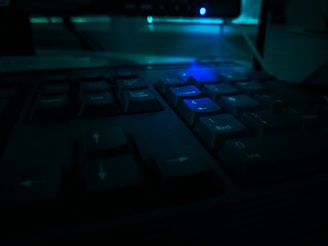 Close-up of a retro computer keyboard with worn keys and a glowing green screen in a cozy room.