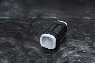 A compact portable speaker with water droplets, hinting at its waterproof feature.
