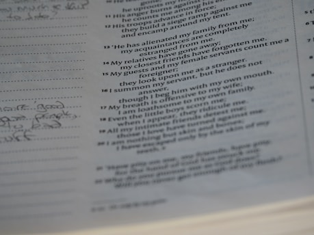 A close-up view of an open book showing printed text on the right side with handwritten notes on lined paper to the left. The text appears to be in paragraph form and may be from a literary or religious source.
