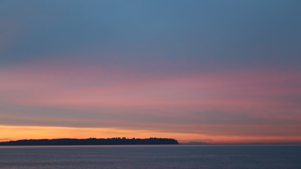 um pôr do sol sobre um corpo de água com uma pequena ilha à distância