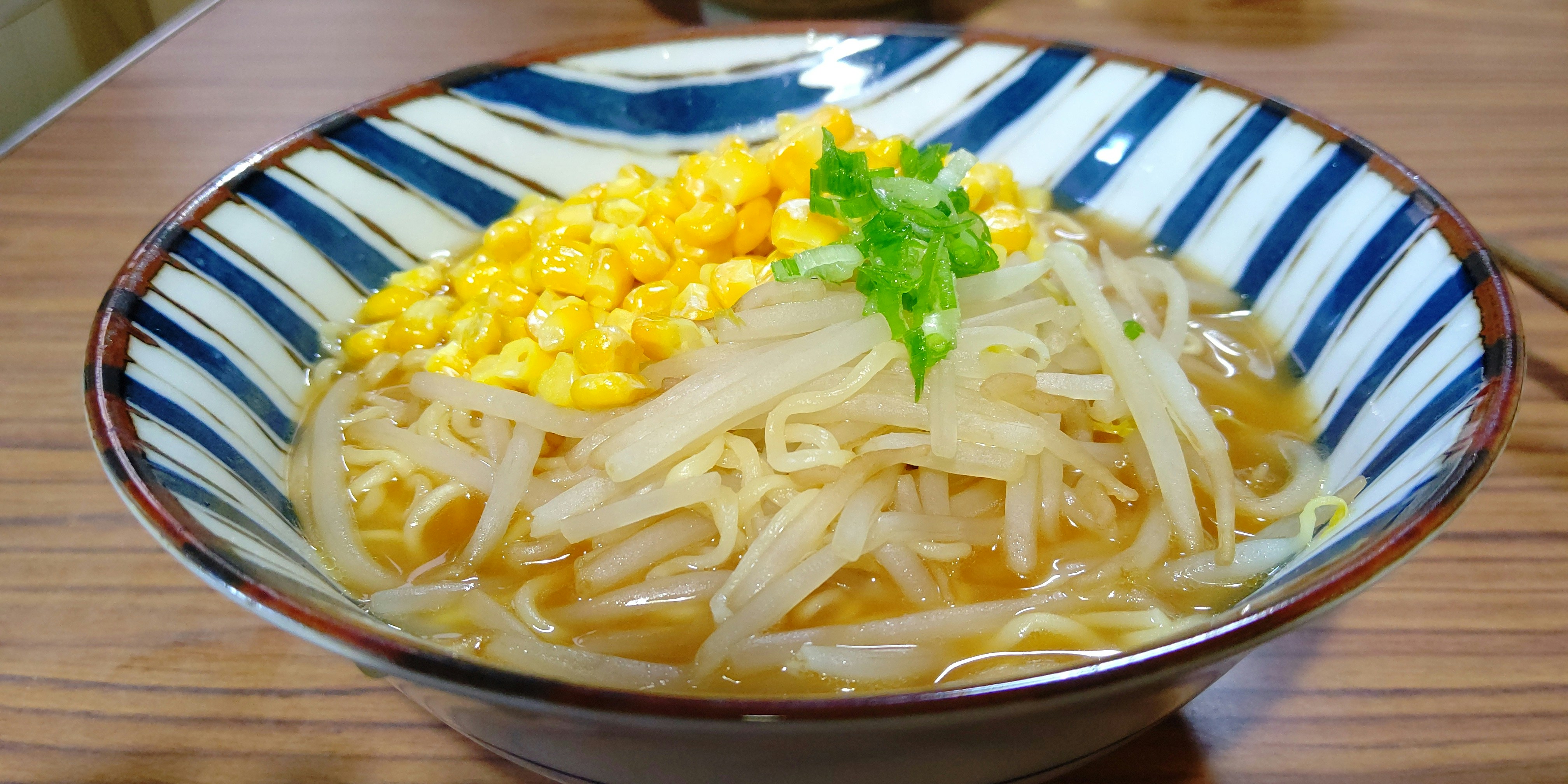 a bowl filled with noodles and corn on top of a wooden table
