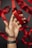 A hand wearing a dark wristband holds a shiny red ribbon against a dark background, with more red ribbons in the background.