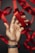 A hand wearing a dark wristband holds a shiny red ribbon against a dark background, with more red ribbons in the background.