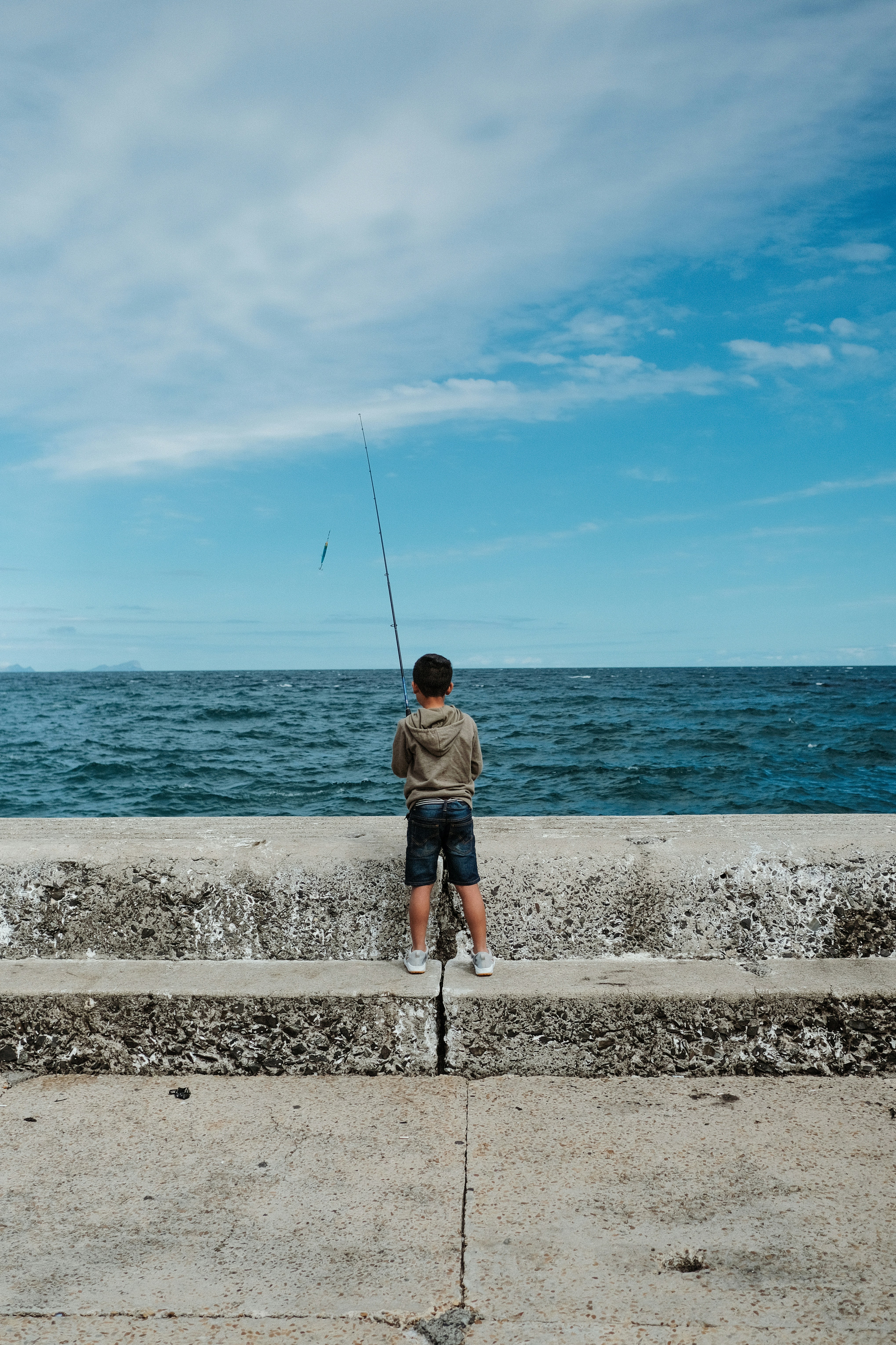 a man sitting on a concrete ledge fishing