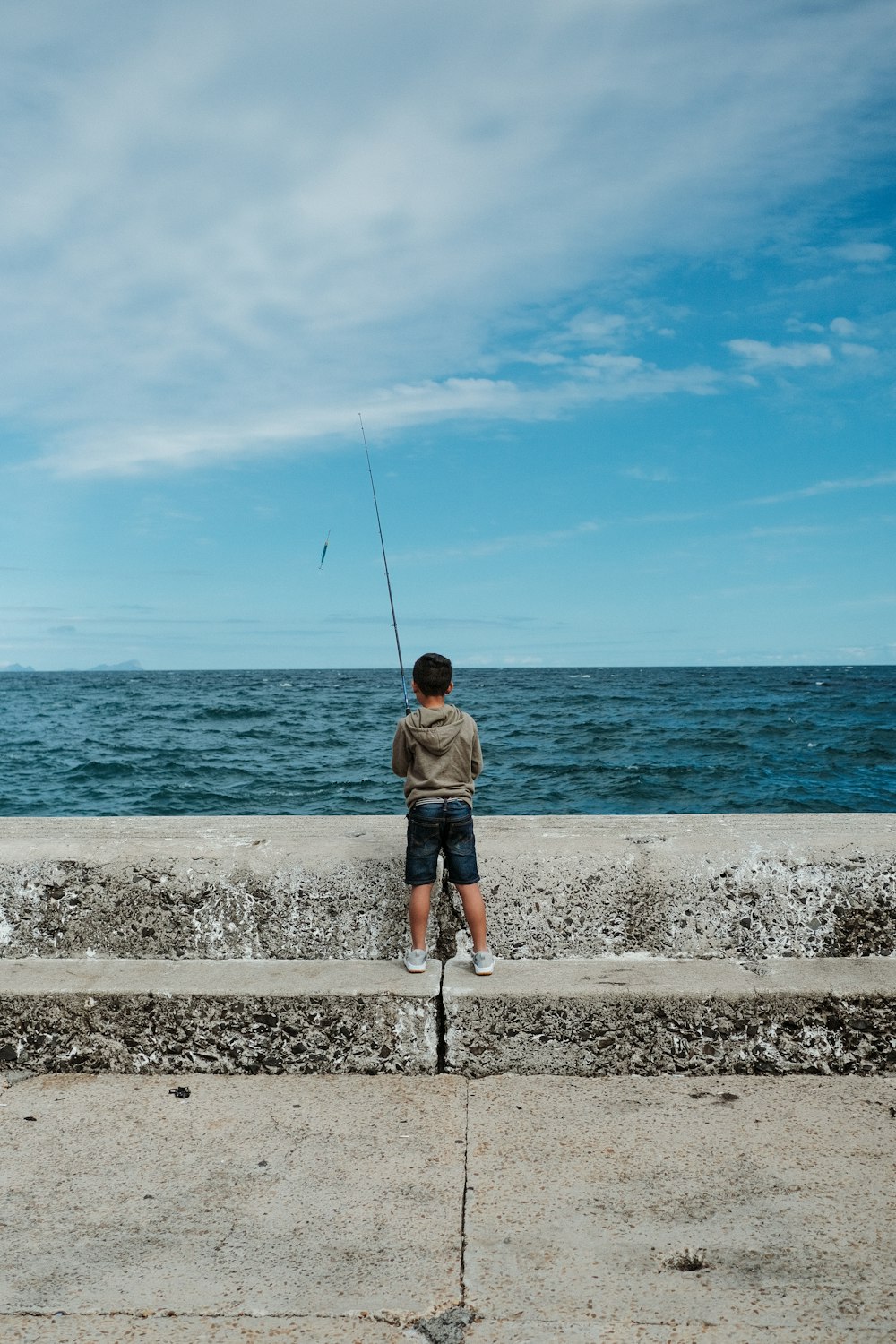 a man sitting on a concrete ledge fishing