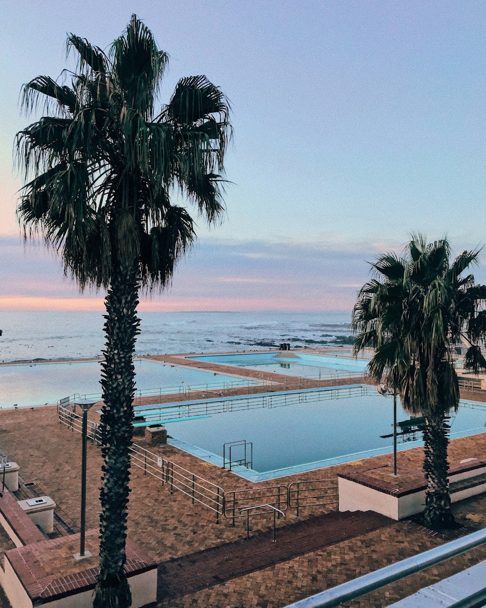 a large swimming pool next to a beach with palm trees