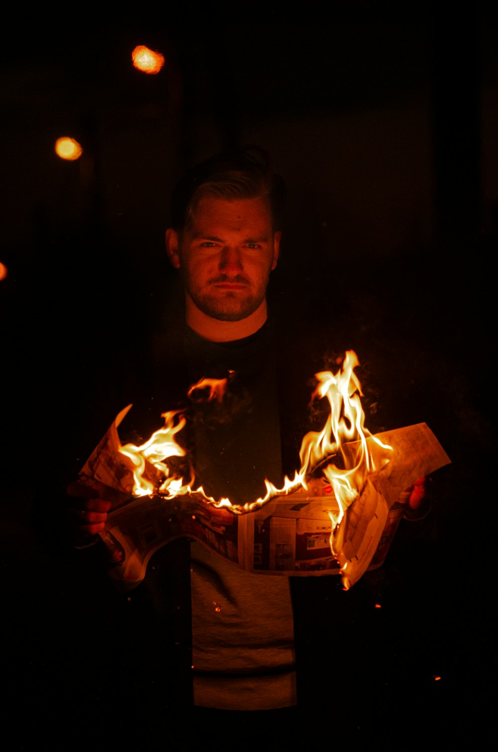 a man standing in the dark holding a piece of paper with fire coming out of