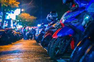 Group of motorcycles riding through city streets illuminated by colorful neon signs at night.