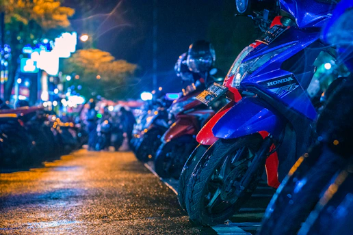 Group of motorcycles riding through city streets illuminated by colorful neon signs at night.