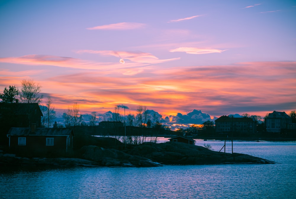 a sunset over a body of water with houses in the background