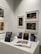 A gallery wall displaying various framed artworks featuring portraits and abstract compositions. Below the artworks, there is a table with a stack of books titled 'Pentimento Alexandre Farto aka Vhils' alongside several smaller prints and an open book displaying some images.