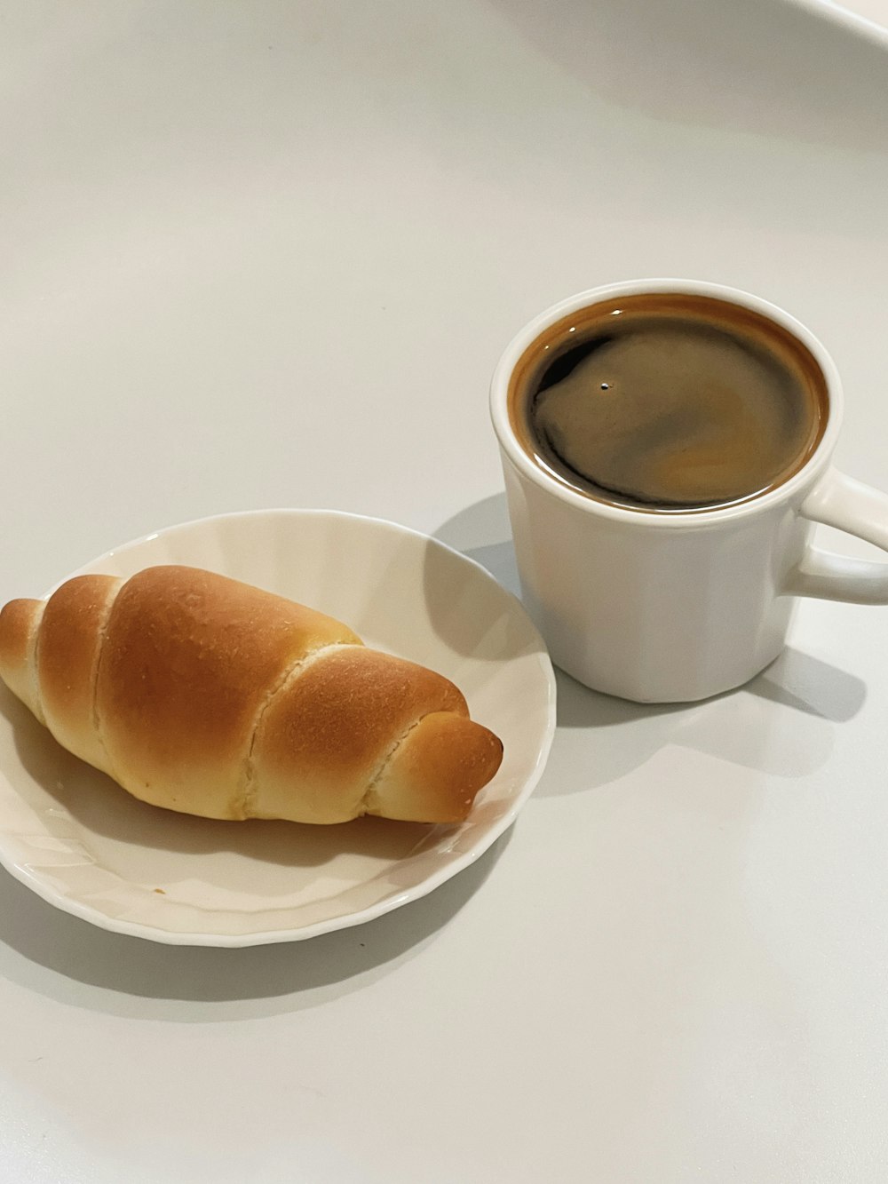 a white plate topped with a piece of bread next to a cup of coffee