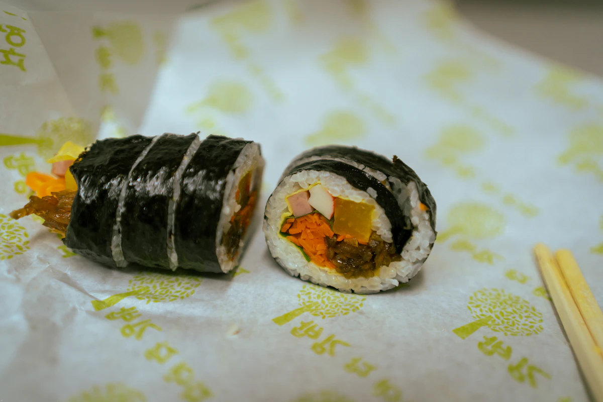 Due rotoli di kimbap posati su carta da asporto stampata, con le bacchette di legno accanto
