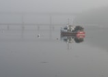 Fishing model boat anchored near a rocky shoreline with early morning mist.