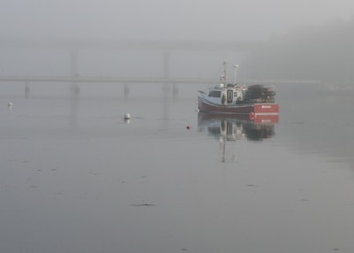 Fishing model boat anchored near a rocky shoreline with early morning mist.