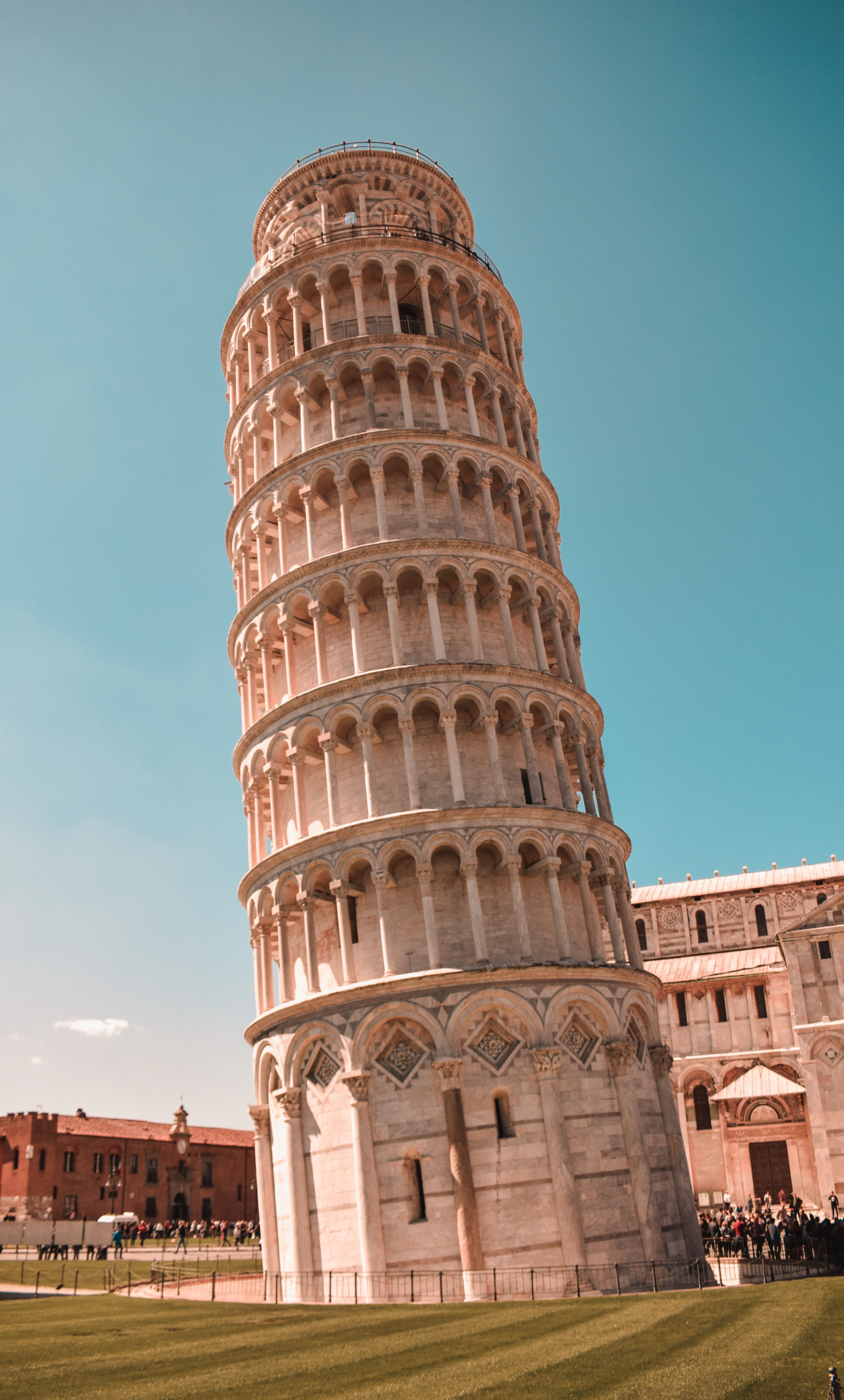 A dramatic low-angle view of the Leaning Tower's tilted arcades glowing warm at dusk beside the cathedral.